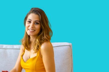 Homem em terno sorrindo e segurando uma prancheta, com um fundo desfocado de casas modernas e uma cidade vibrante ao pôr do sol.