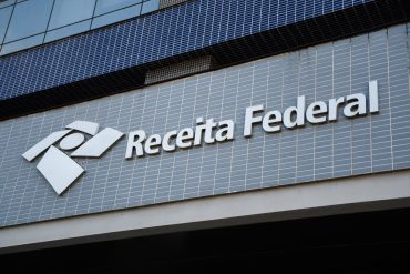 Estudante focado estudando para o concurso Analista Receita Federal, com material digital e livro em destaque.