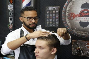 Barbeiro profissional cortando cabelo com tesoura e pente, em ambiente de barbearia moderna.